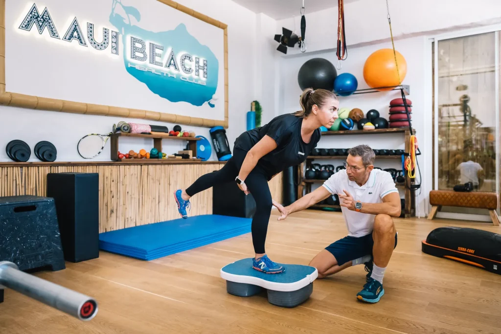 Stefan Hornburg begleitet eine Kundin bei einer einbeinigen Übung auf dem Balance-Board