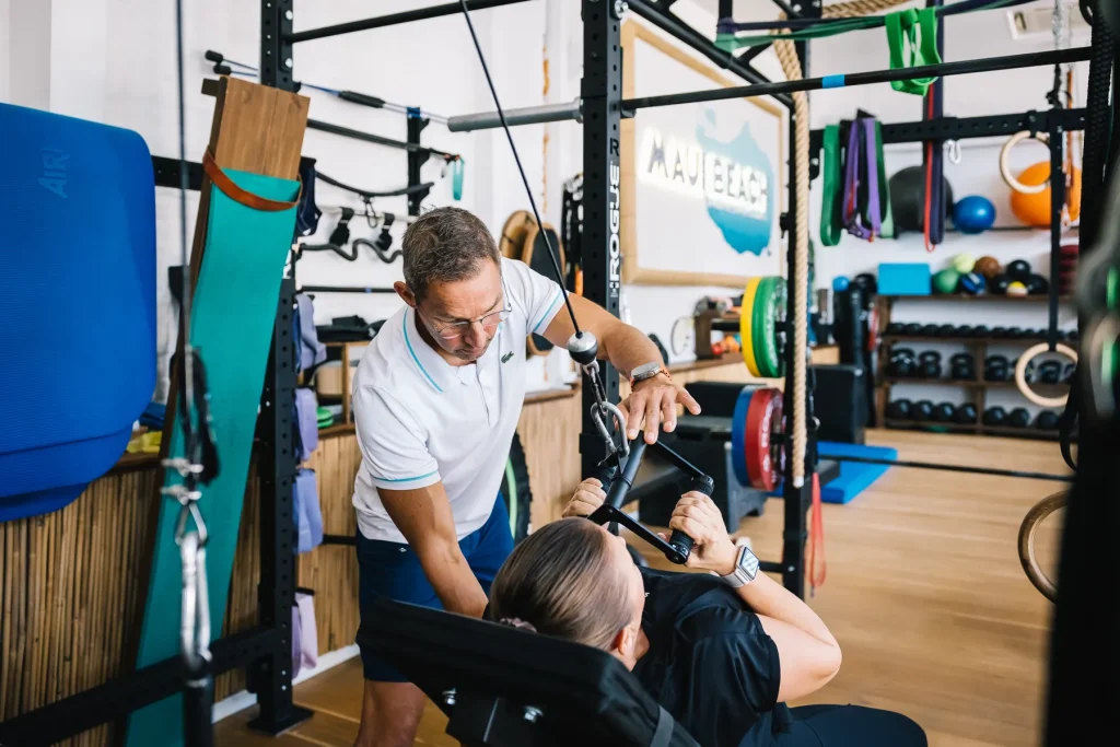 Stefan Hornburg korrigiert eine Kundin bei einer Zugübung auf der Trainingsbank